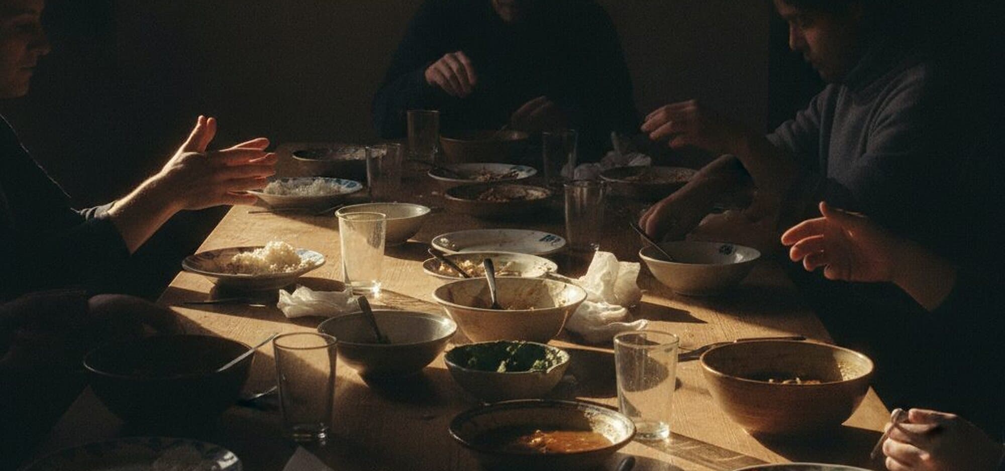 A long table after a shared meal at the church in Herten, hands passing dishes in warm light